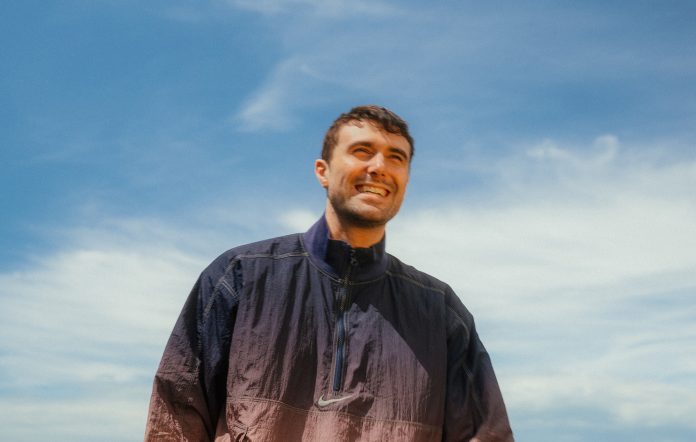 Fred Again.. pictured in a windbreaker against a blue sky, photo by press